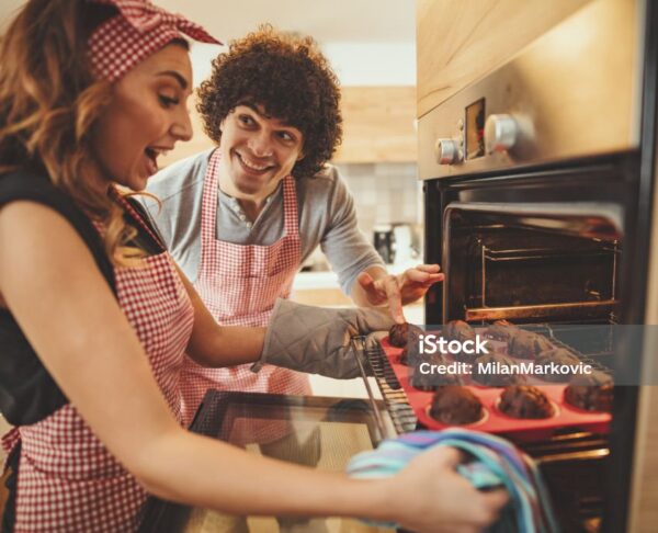 Young happy couple is pulling baked chocolate muffins from the oven.